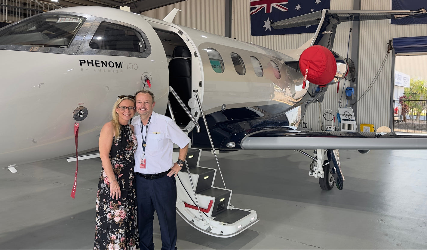 Two people standing in front of a Phenom aircraft inside an airport hangar with Australian flags on the wall.